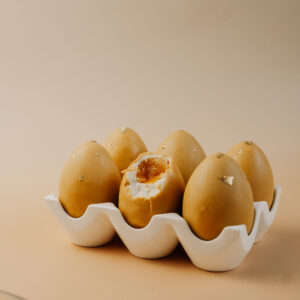 Bitten egg-shaped dessert revealing a white vanilla mousse exterior and a bright orange passion fruit centre.